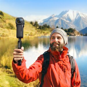A person holding a camera with a 360-degree lens. The camera is attached to a selfie stick. The person is standing in front of a scenic view of a mountain range, best camcorder, Insta360 ONE RS 1-Inch 360