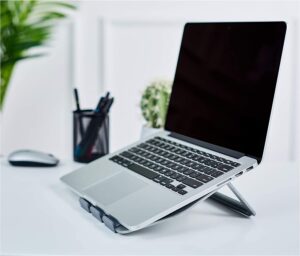 A laptop computer sitting on top of a laptop stand on a white table. The laptop is open and the screen is blank. The mouse is next to the laptop. - productcruise.com