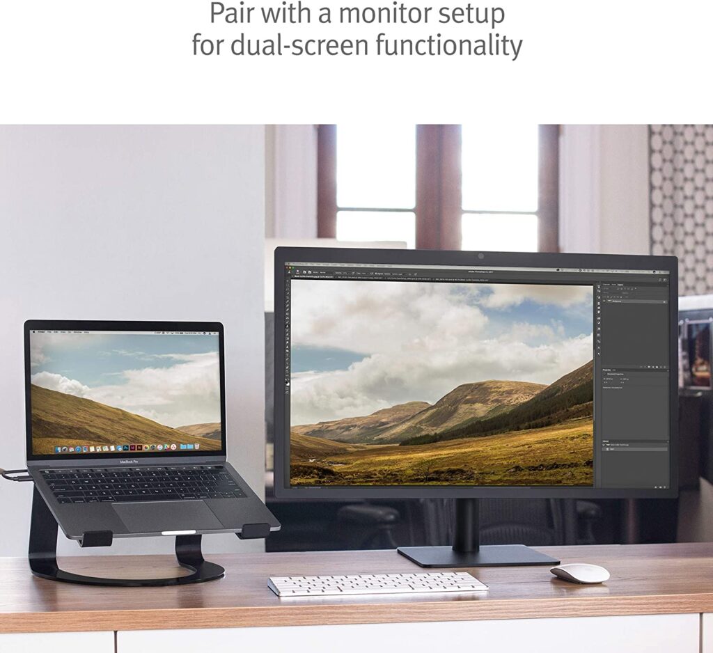 A laptop sitting on a laptop stand next to a monitor. The laptop stand is black and has a curved design. The laptop is open and the monitor is turned on. The text on the image says "Pair with a monitor setup for dual-screen functionality." - productcruise.com, Twelve South Curve Stand for MacBook
