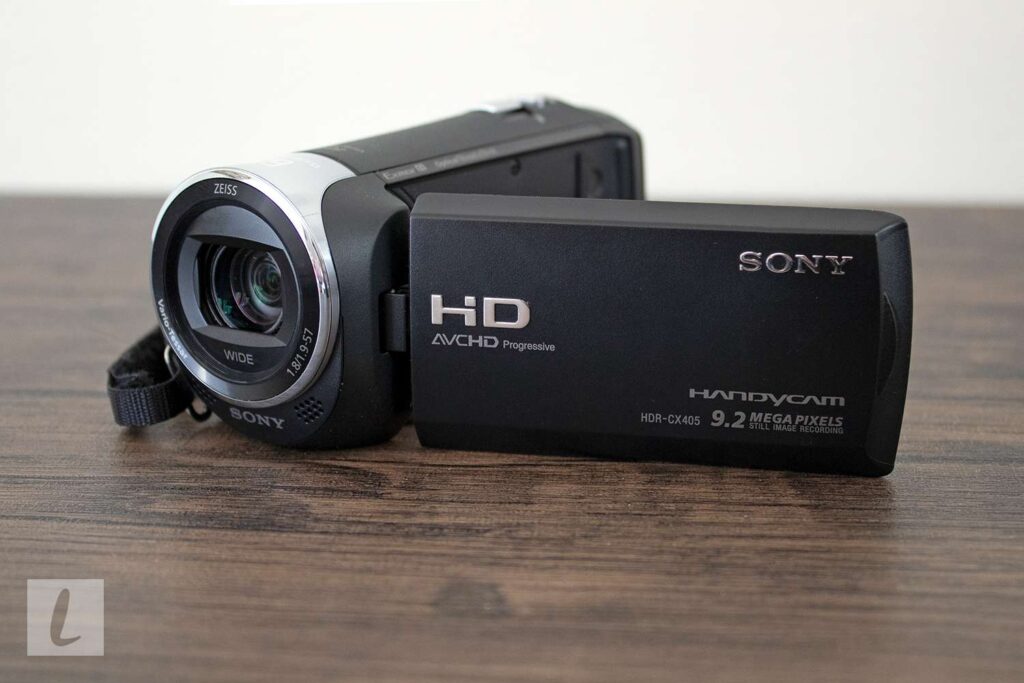 A Sony Handycam HDR-CX405 sits on a wooden table, capturing video with its ZEISS lens, best camcorder, Sony - HDRCX405